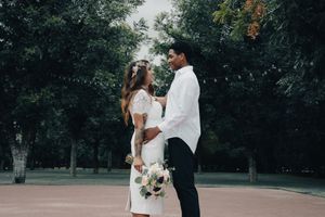 Couple in wedding attire standing face to face in a lush green park, bride holding a colorful bouquet.