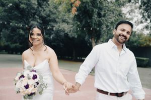 Happy bride and groom walk hand in hand holding wedding bouquet outdoors.