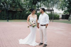 Bride and groom holding hands in a park, bride in white mermaid gown holding bouquet, groom in white shirt and khakis.