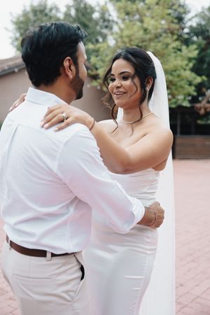 Bride in white gown and veil dances with groom outdoors on wedding day.