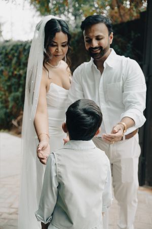 Bride and groom interact warmly with their young son on a patio surrounded by greenery.