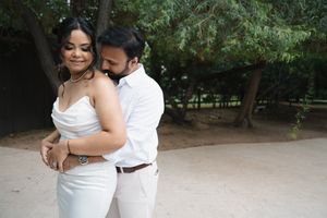 Couple in white embracing outdoors near trees during wedding photo session.