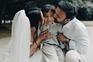 Bride and groom kissing their young son on the cheeks simultaneously in an outdoor setting.