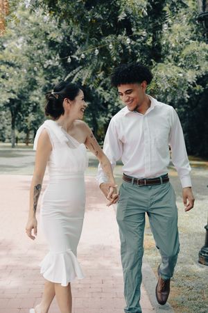 Smiling interracial couple holding hands and walking together along a brick path in a green park.