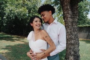 Happy interracial couple embracing and smiling together near a tree in a sunny green park.