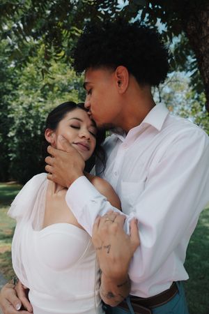 Groom tenderly kisses bride on the cheek while embracing her in a sunlit garden.