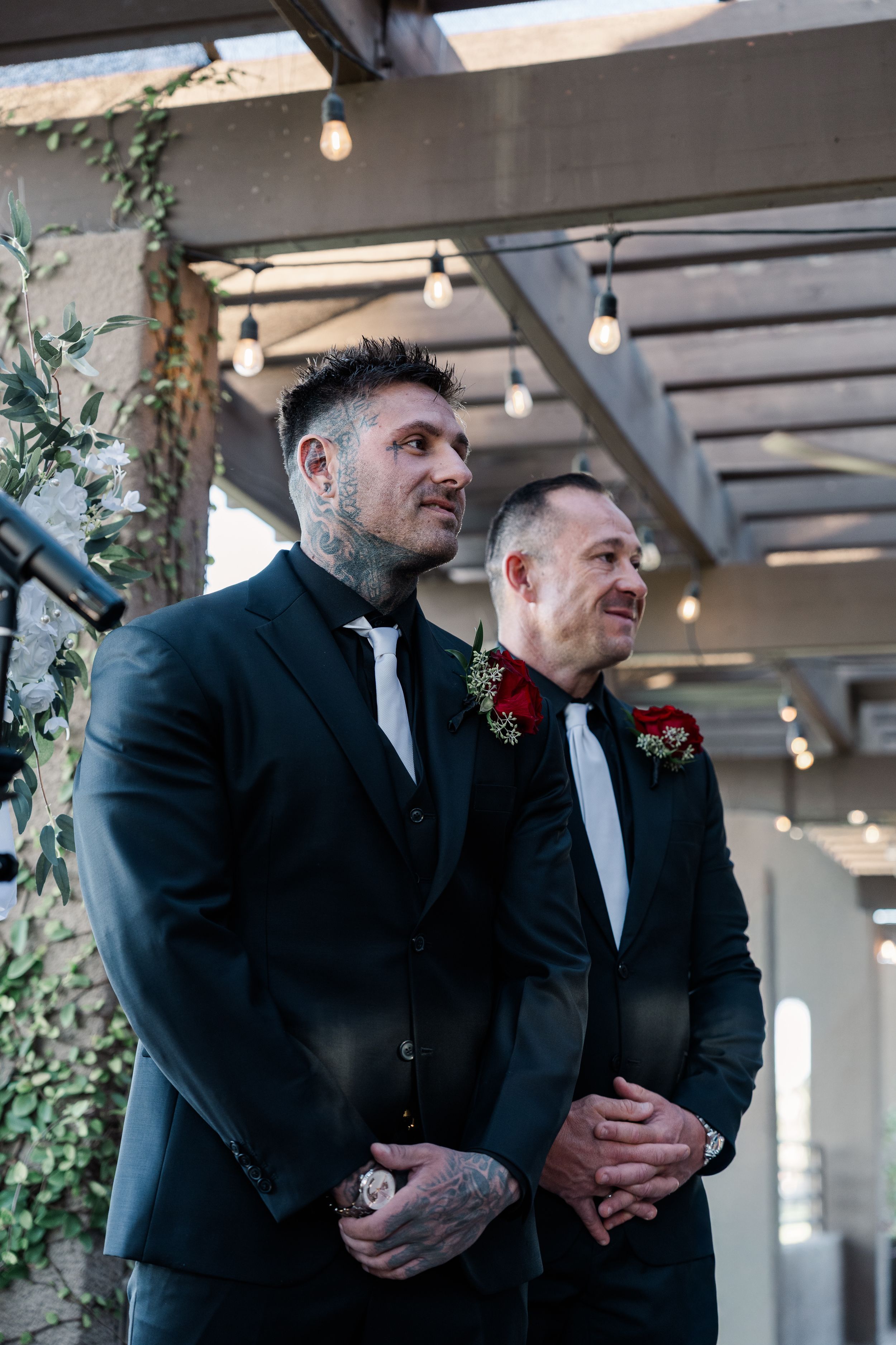 Two men in black suits with red boutonnieres stand at the altar awaiting the bride.