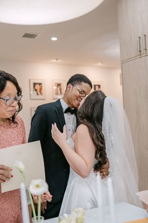 Groom in tuxedo shares tender moment with bride in white dress during intimate wedding ceremony.