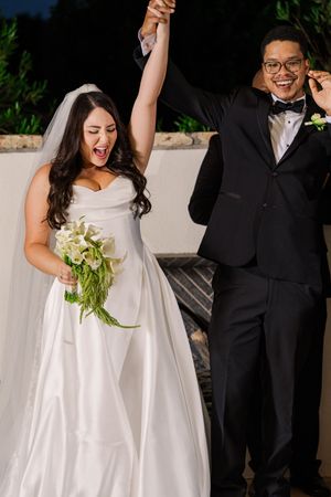 Excited bride and groom celebrate with raised hands after wedding ceremony at night.