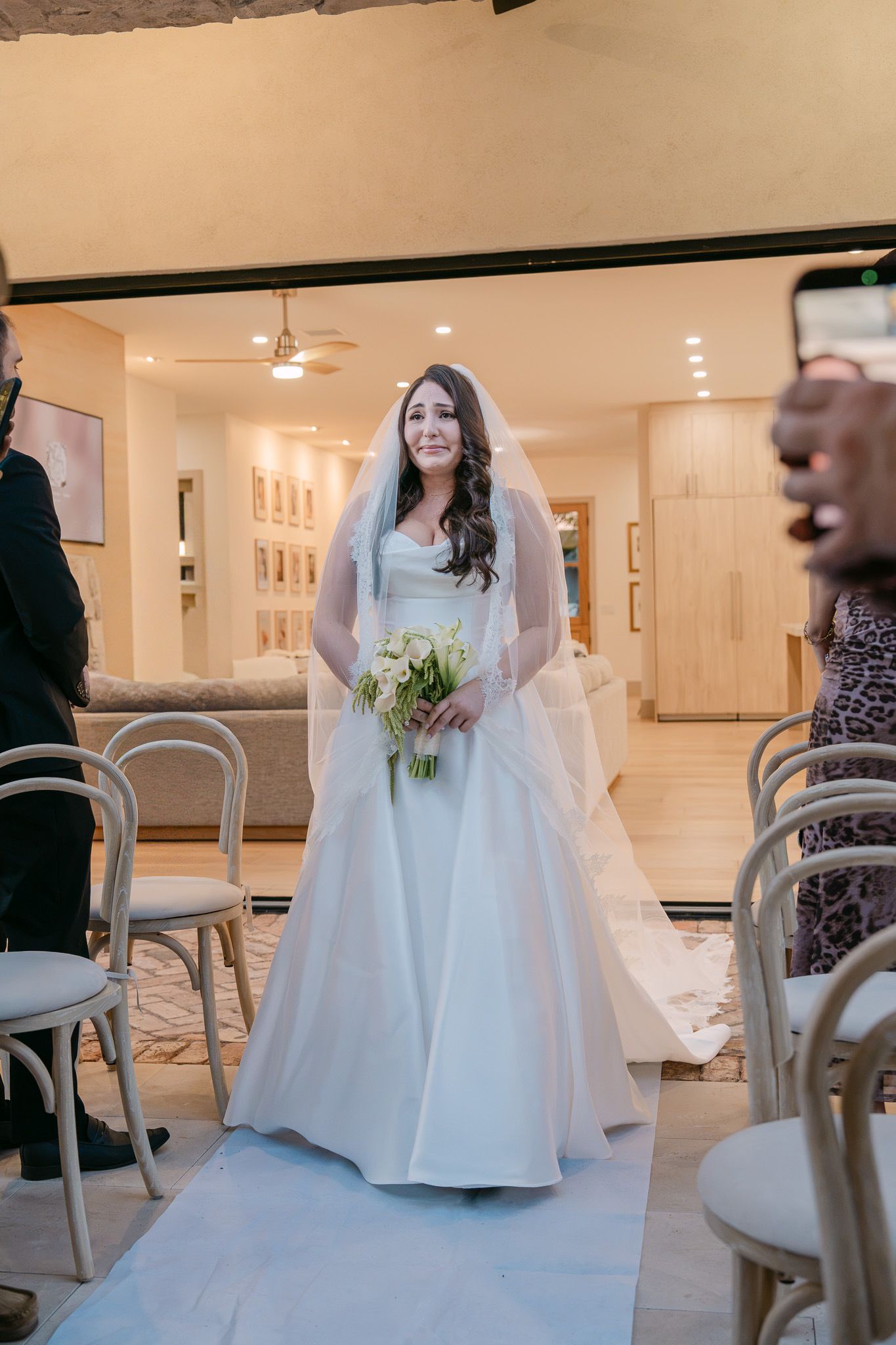 Elegant bride in a classic white ballgown and veil walks down the aisle holding white flowers.