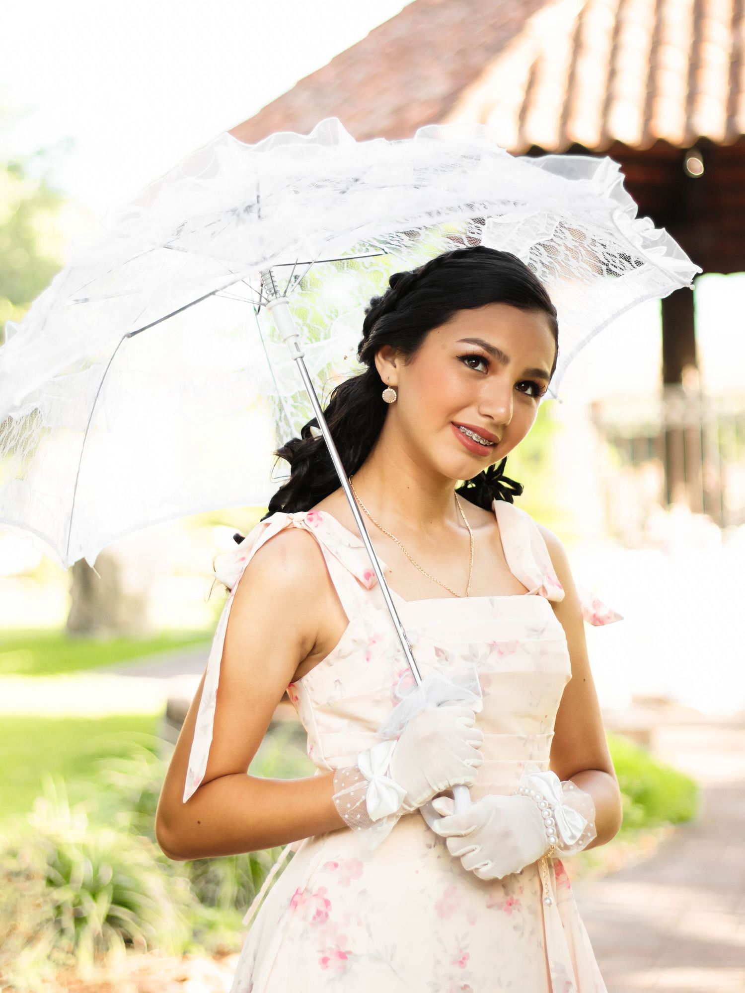 Young woman in floral dress and white lace gloves holding a white parasol umbrella outdoors.