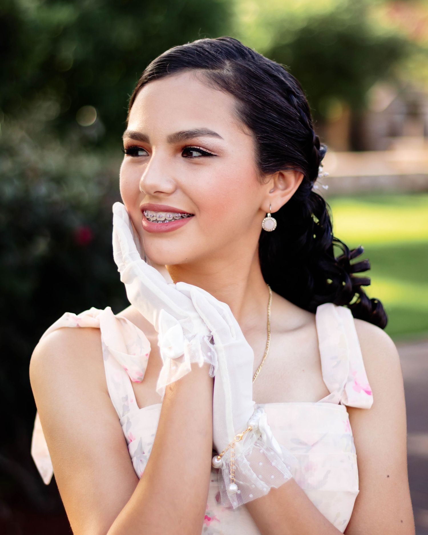 Young woman in floral dress and white lace gloves holding a white parasol umbrella outdoors.