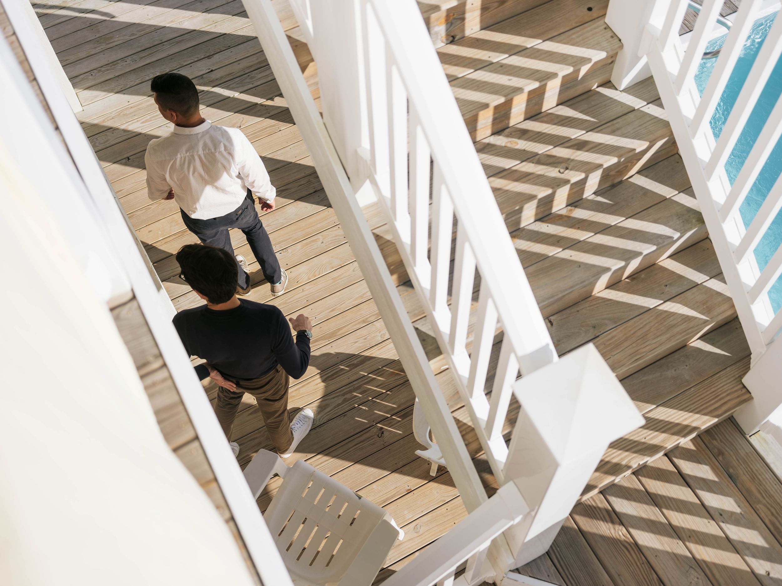 Aerial view of two people walking on a wooden deck with white railings and herringbone pattern flooring.