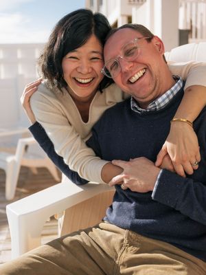 A joyful couple embracing and laughing together outdoors on a sunny deck, sharing a warm and happy moment.
