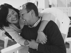 A joyful couple laughing and embracing outdoors in a candid black and white portrait photo.