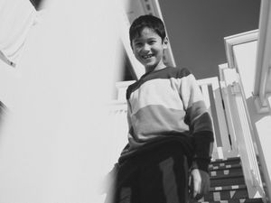 Smiling young boy in a striped sweatshirt standing on outdoor steps, captured in black and white photography.