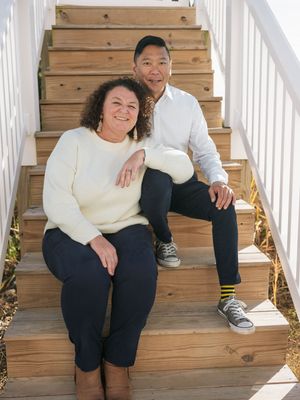 A smiling couple sitting together on wooden outdoor stairs, woman in cream sweater and man in white shirt.