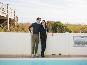 Couple posing together by a pool with a white fence and natural dunes in the background outdoors.