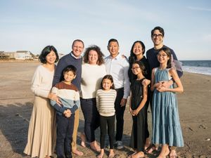 A joyful multigenerational family poses together on a sunny beach, smiling warmly for a group portrait.
