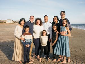 A happy multigenerational family smiling together on a sandy beach during golden hour.