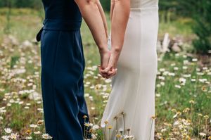 Couple holding hands in a flower field, wearing navy suit and white wedding dress.