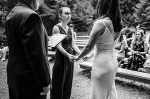 Black and white photo of a wedding officiant holding hands with bride during outdoor ceremony.