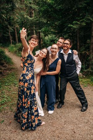 Group of five friends posing for a selfie on a forest path, dressed in formal attire for a wedding celebration.