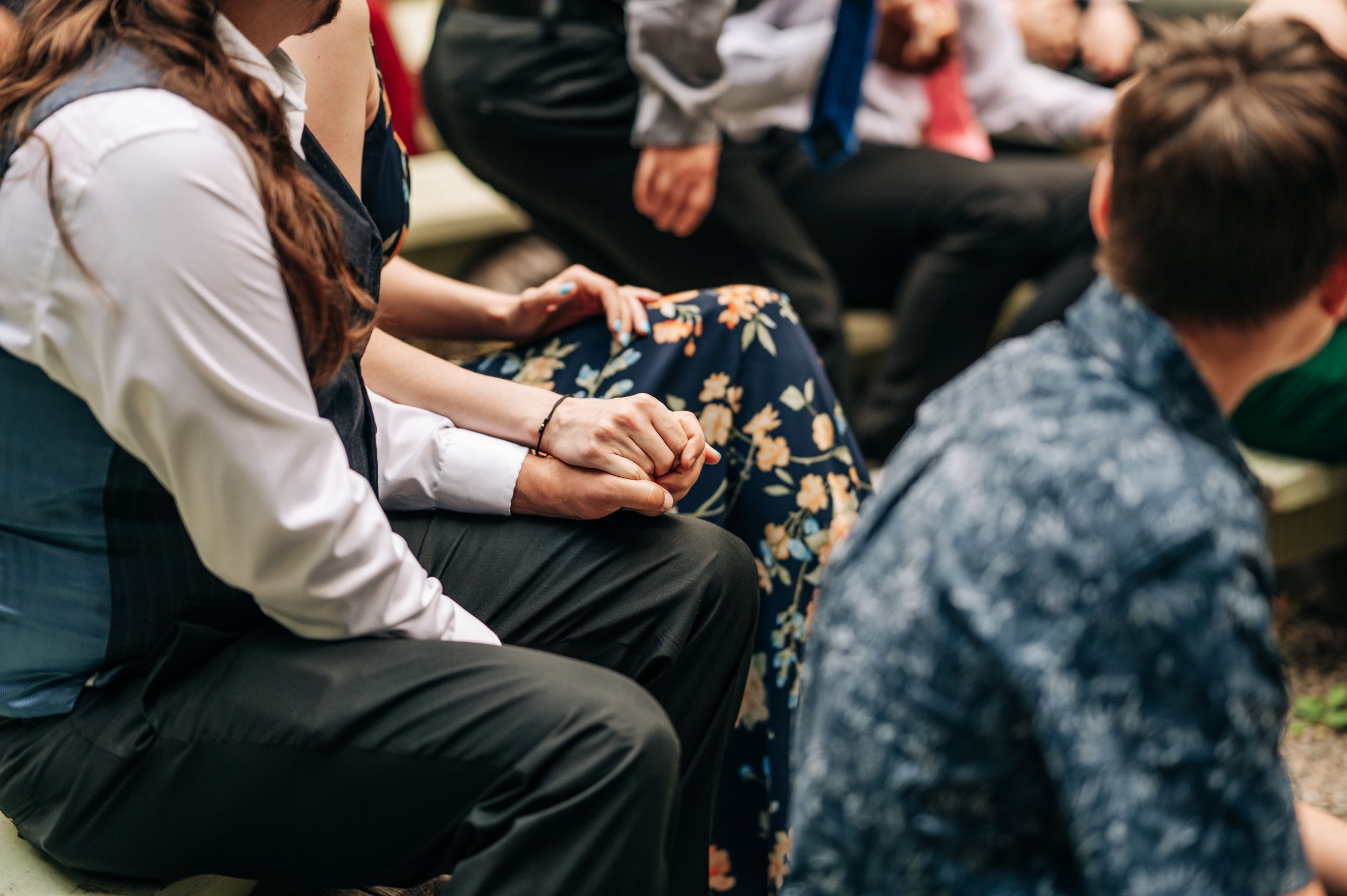 Wedding guests sit closely together outdoors, holding hands during an intimate garden ceremony.
