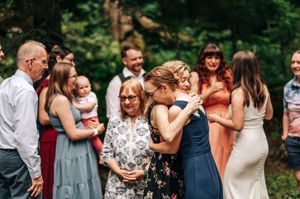 Wedding guests embrace and celebrate with the newlyweds during an outdoor forest ceremony.