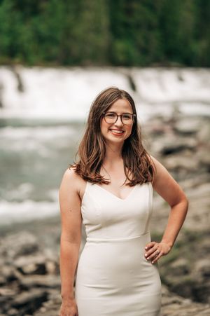 Smiling bride in white dress poses in front of a waterfall outdoors.