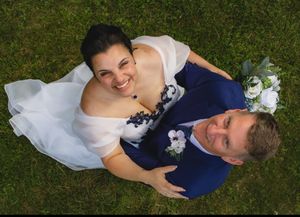 Aerial view of smiling bride and groom lying on grass, bride holding white bouquet.