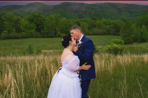 Bride and groom share a romantic kiss in a field with stunning mountain sunset backdrop, bride in white gown.