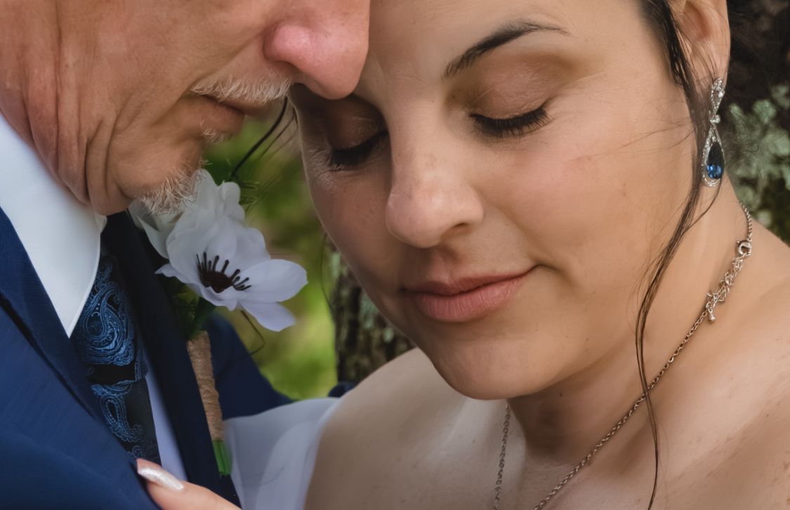 Close-up of a bride and groom sharing an intimate moment, with a white flower boutonniere visible on his suit.