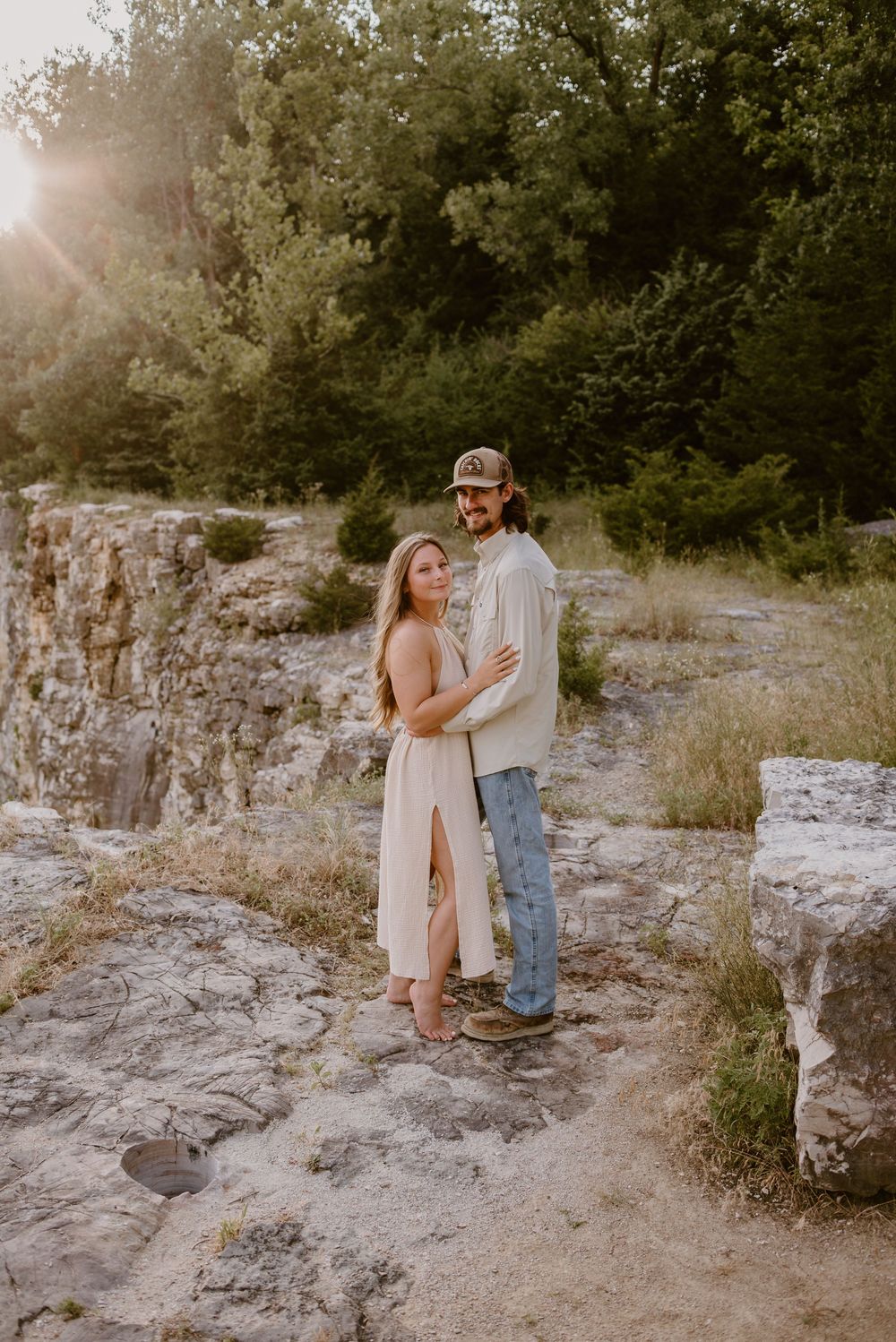 A couple embraces on rocky terrain during a golden hour photoshoot.