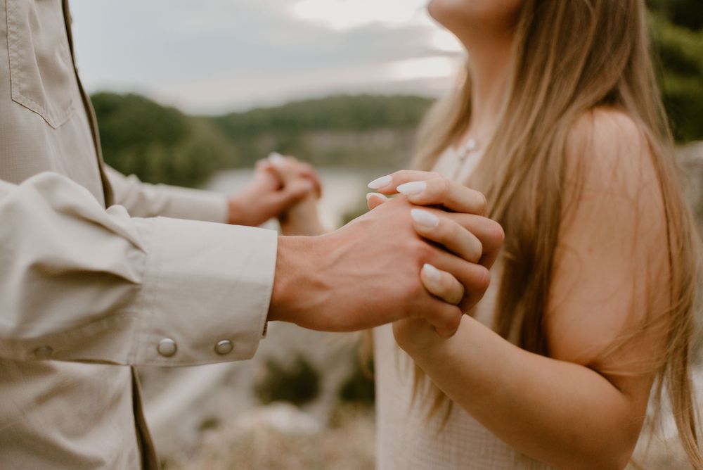 A romantic engagement photo shoot in warm autumn light with hands clasped together.