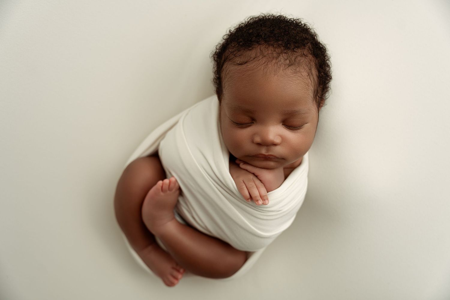 Peaceful newborn baby swaddled in white wrap sleeping on soft white background in professional portrait.