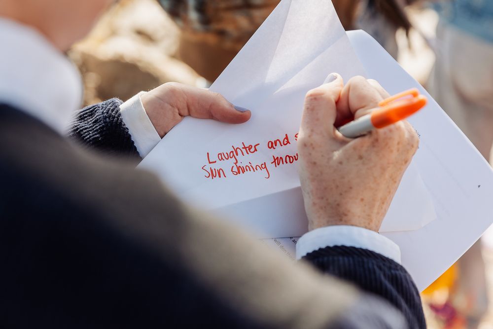 Person writing wedding wishes with an orange marker on a white card, with text reading Laughter and love.
