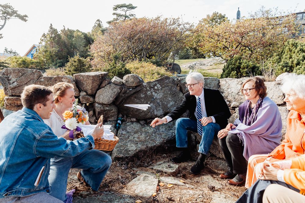 Four people sit on stone steps outdoors, sharing food and conversation in a scenic garden setting on a sunny day.