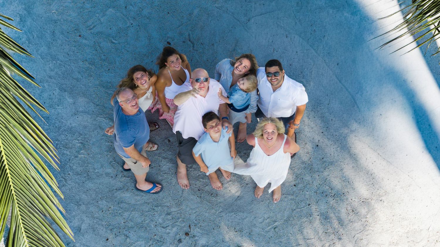 Aerial view of a happy multigenerational family group standing together on sandy beach, smiling up at camera.