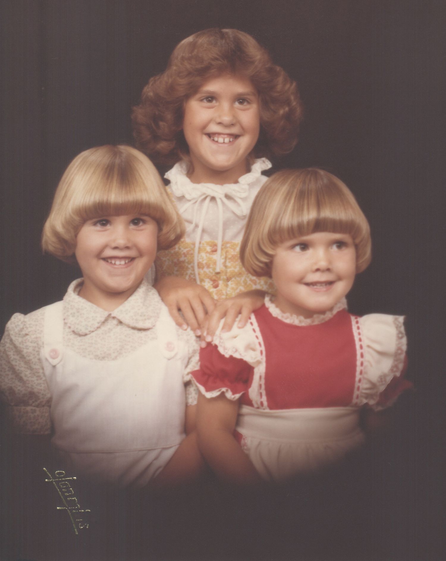 Vintage portrait of three young girls in formal dresses, two blonde sisters in front and a curly redhead behind.