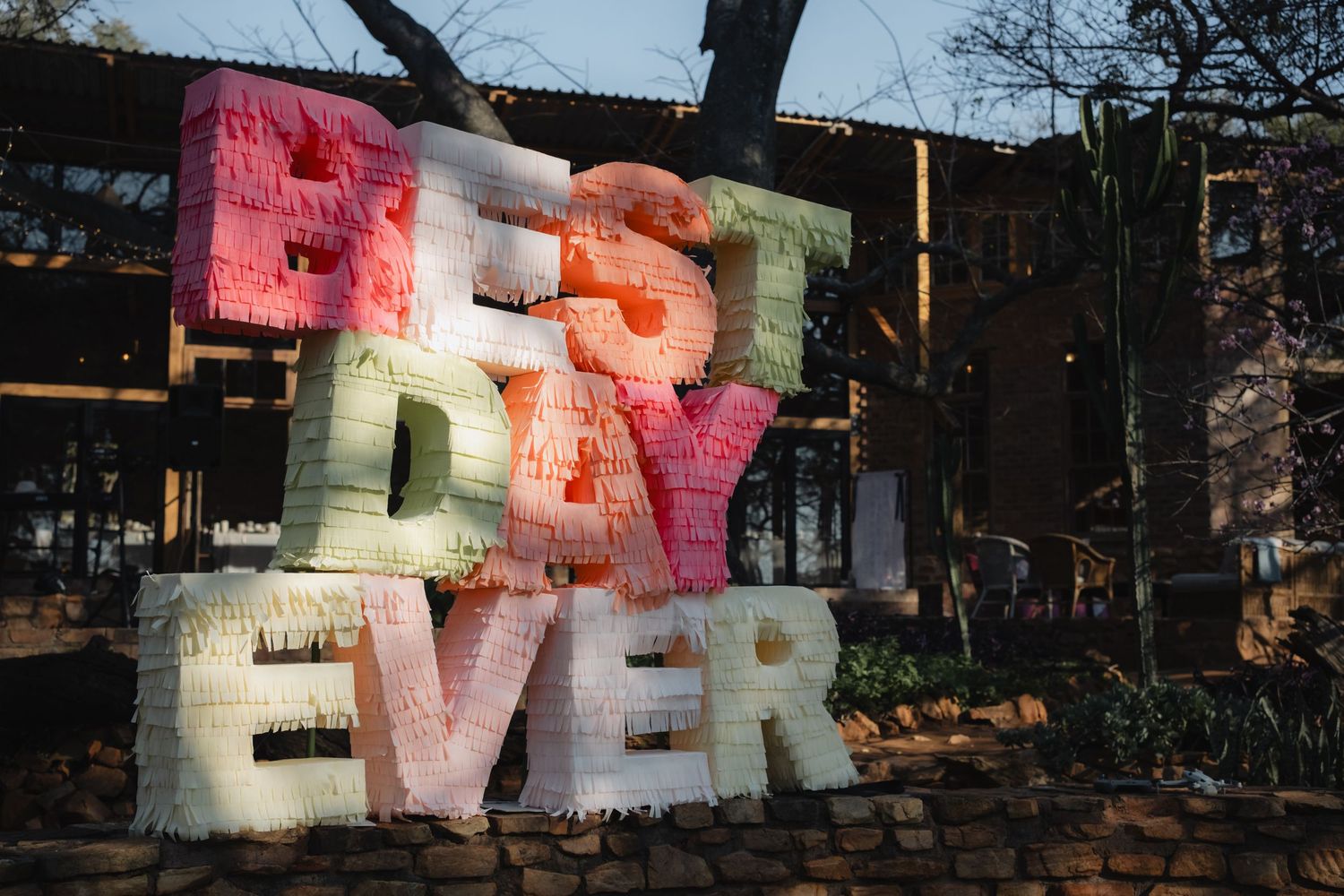 Colorful 3D letters spelling Best Day Ever displayed outdoors at a rustic venue with trees in background.