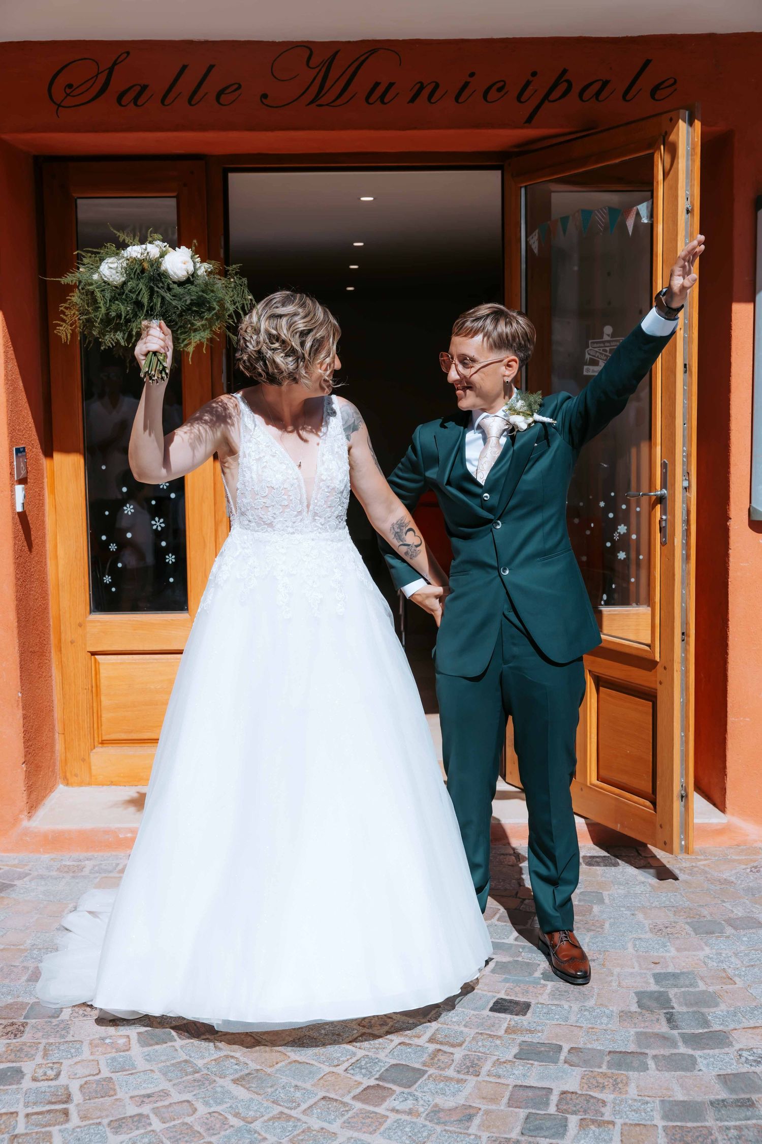 Bride and groom share their first kiss at an outdoor wedding ceremony surrounded by guests and lush greenery.
