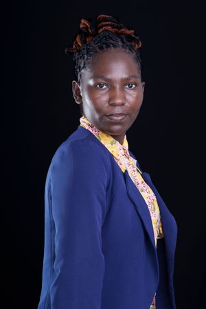 Professional woman in blue blazer and yellow shirt poses against black background.
