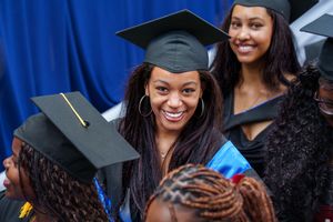Smiling graduate in cap and gown poses with peers at graduation ceremony.