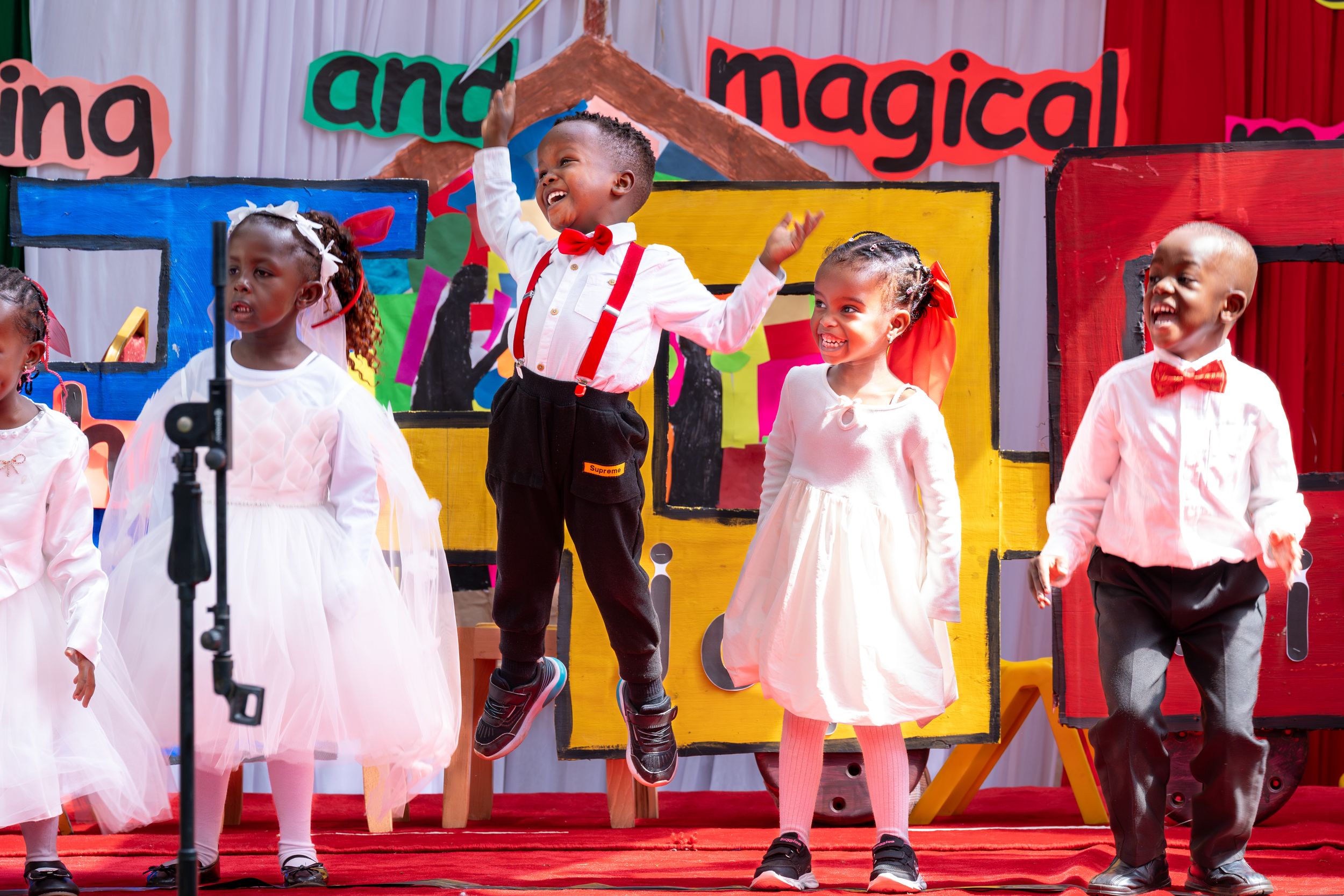 Young children perform on stage in formal attire at school recital.