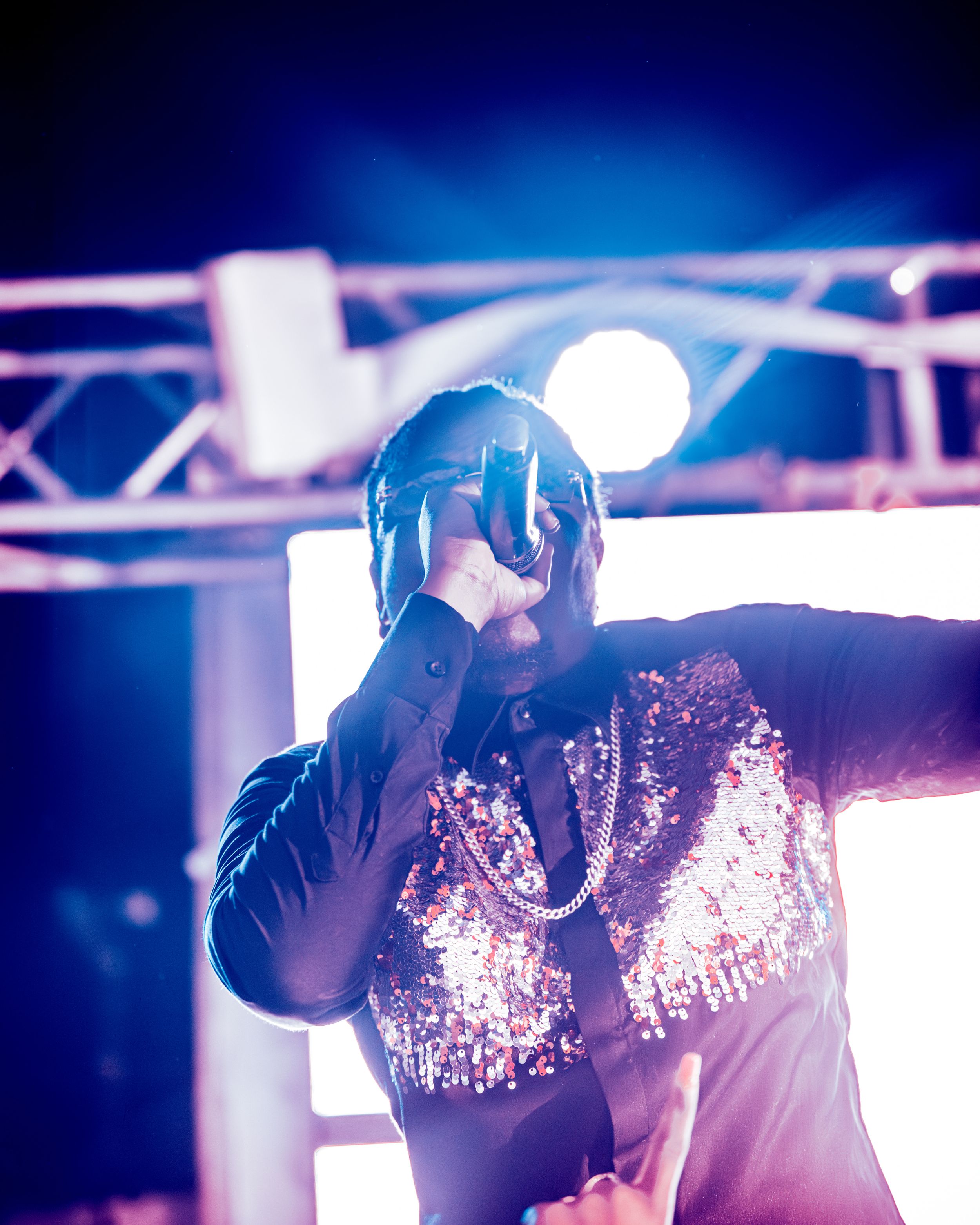 Performer in a sequined jacket holding a microphone under dramatic stage lighting at a live event.