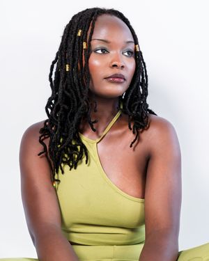 Young woman with long black locs and gold beads wearing olive green top.