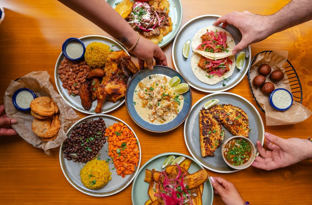Overhead view of a festive table spread with colorful Mexican dishes, tacos, rice, beans, and sauces shared among friends.