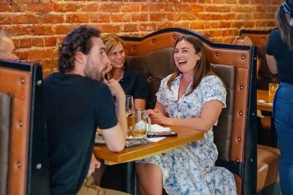 Two people laughing and enjoying a meal together at a rustic restaurant with exposed brick walls.