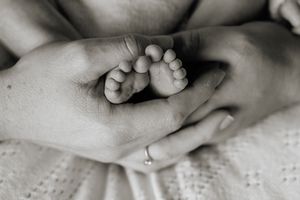 Black and white photo of tiny newborn baby feet cradled gently in loving adult hands.